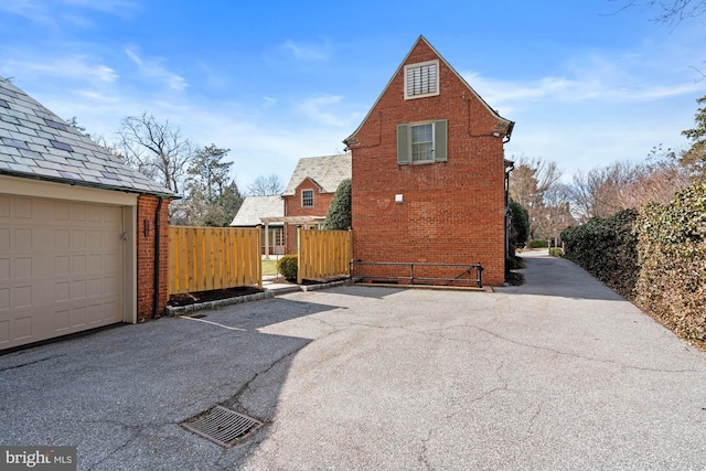 view of side of home with a garage, driveway, fence, a high end roof, and brick siding