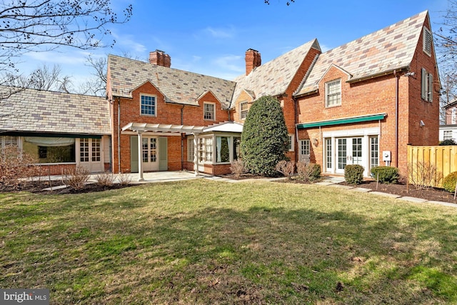 rear view of property featuring a high end roof, french doors, brick siding, and a lawn