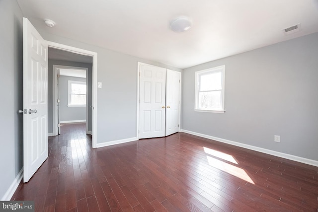 unfurnished bedroom with baseboards, visible vents, dark wood finished floors, and a closet