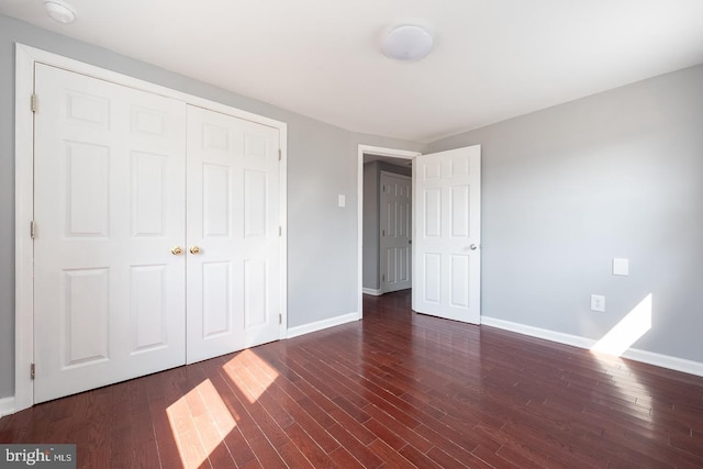 unfurnished bedroom with dark wood-style floors, a closet, and baseboards