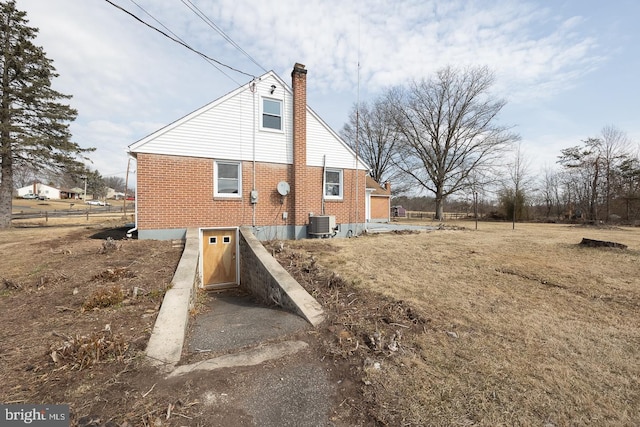 view of home's exterior with central air condition unit, a chimney, and brick siding