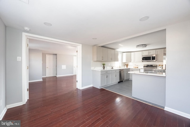 kitchen featuring dark wood finished floors, stainless steel appliances, tasteful backsplash, light countertops, and baseboards