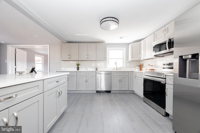 kitchen featuring tasteful backsplash, appliances with stainless steel finishes, light countertops, light wood-type flooring, and a sink