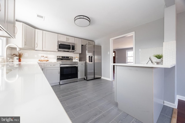 kitchen featuring visible vents, wood tiled floor, stainless steel appliances, light countertops, and backsplash