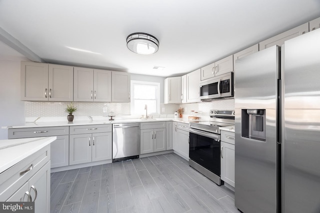 kitchen with light countertops, appliances with stainless steel finishes, wood finish floors, and backsplash