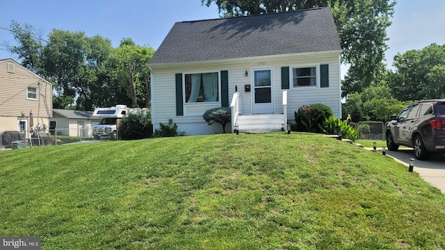 view of front facade featuring roof with shingles, a front yard, and fence