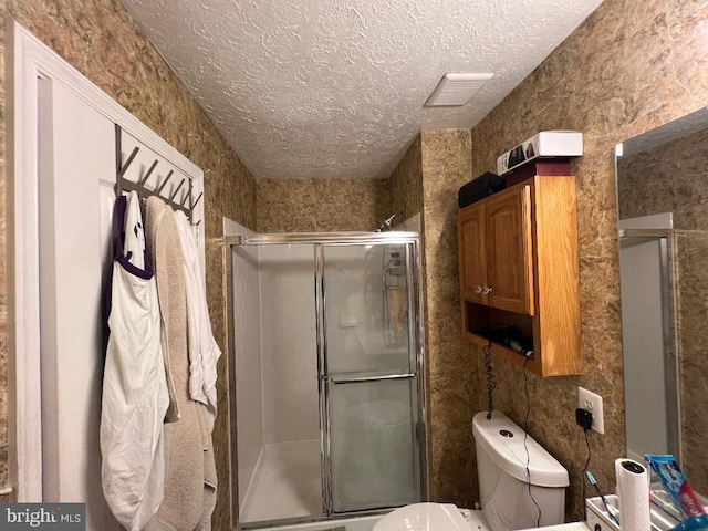 full bathroom featuring visible vents, toilet, a textured ceiling, and a shower stall