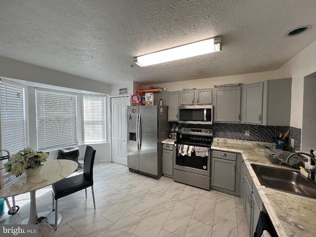 kitchen with marble finish floor, stainless steel appliances, gray cabinets, decorative backsplash, and a sink