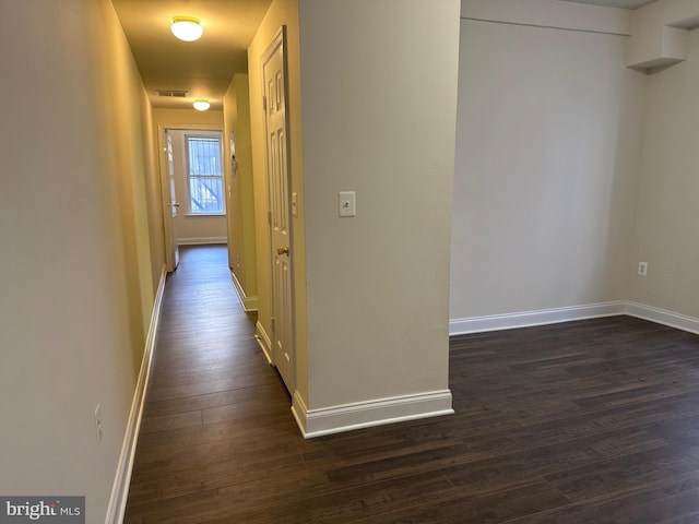 hall featuring dark wood-type flooring, visible vents, and baseboards