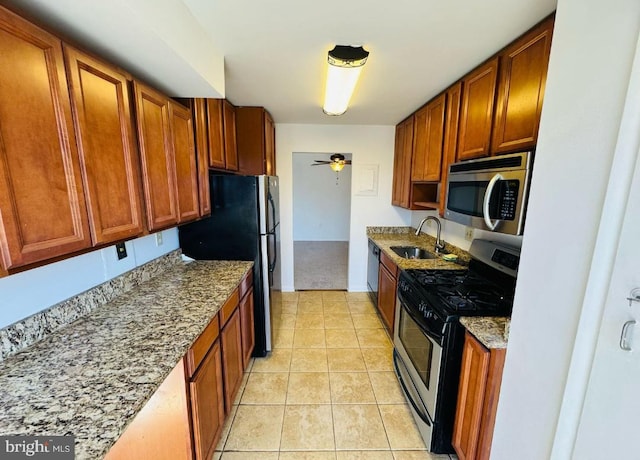 kitchen with appliances with stainless steel finishes, light tile patterned flooring, a sink, ceiling fan, and light stone countertops