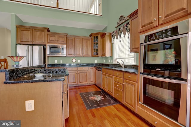 kitchen featuring glass insert cabinets, dark stone countertops, light wood-style flooring, stainless steel appliances, and a sink