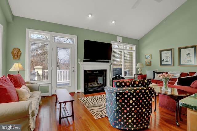 living room featuring plenty of natural light, lofted ceiling, a fireplace with flush hearth, and wood finished floors