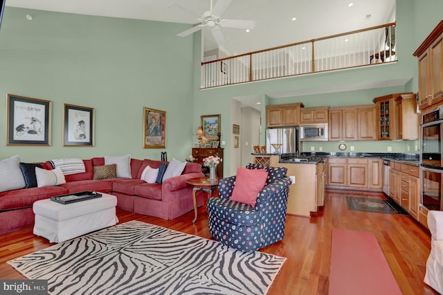 living room featuring ceiling fan, wood finished floors, and a towering ceiling