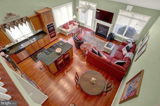 living area featuring a fireplace with flush hearth, a ceiling fan, and wood finished floors