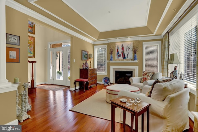 living room with ornamental molding, a tray ceiling, hardwood / wood-style floors, a glass covered fireplace, and baseboards