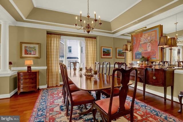 dining room featuring a tray ceiling, wood finished floors, ornamental molding, and ornate columns