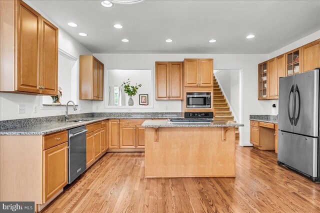 kitchen featuring a center island, glass insert cabinets, appliances with stainless steel finishes, a kitchen breakfast bar, and a sink