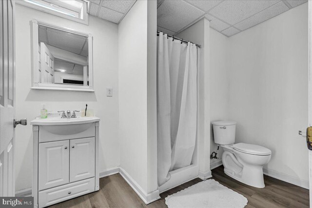 bathroom featuring toilet, wood finished floors, baseboards, and a drop ceiling