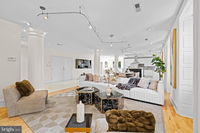 living area with light wood-style flooring, rail lighting, visible vents, and ornate columns