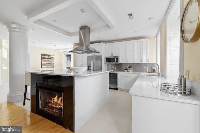 kitchen with beverage cooler, visible vents, appliances with stainless steel finishes, island exhaust hood, and a sink