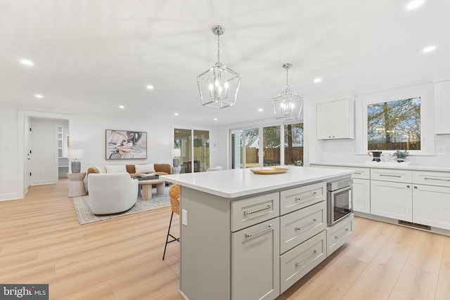 kitchen featuring light wood-style flooring, recessed lighting, open floor plan, light countertops, and built in microwave