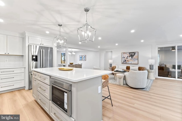 kitchen featuring light wood-style flooring, appliances with stainless steel finishes, open floor plan, light countertops, and a kitchen bar