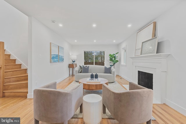 living room with recessed lighting, a fireplace, baseboards, stairs, and light wood-style floors