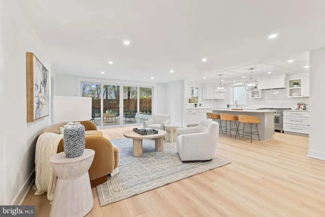 living room featuring a chandelier, recessed lighting, baseboards, and light wood finished floors