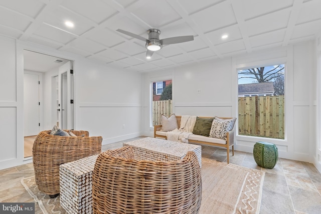 sitting room featuring baseboards, coffered ceiling, a ceiling fan, a decorative wall, and recessed lighting