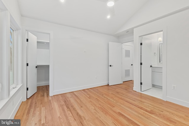 unfurnished bedroom with vaulted ceiling, baseboards, a walk in closet, and light wood-style floors