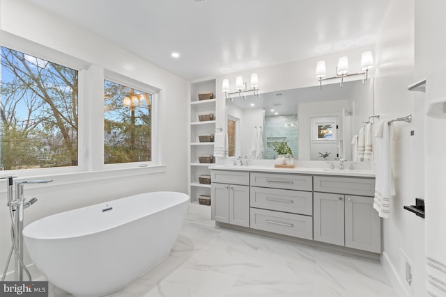 full bath featuring double vanity, marble finish floor, a freestanding bath, and a sink