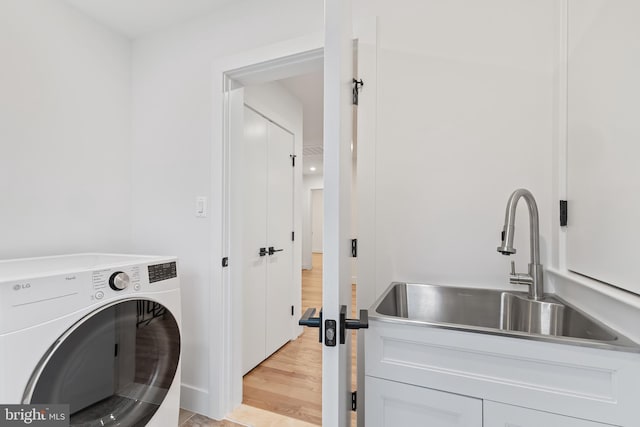 laundry area with light wood-type flooring, washer / dryer, laundry area, and a sink