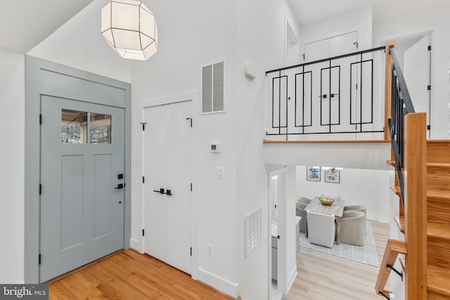 entryway featuring light wood-style flooring, a towering ceiling, visible vents, stairs, and baseboards