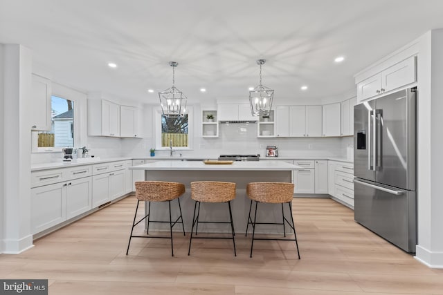 kitchen with a breakfast bar area, a center island, light wood-type flooring, white cabinetry, and high end fridge