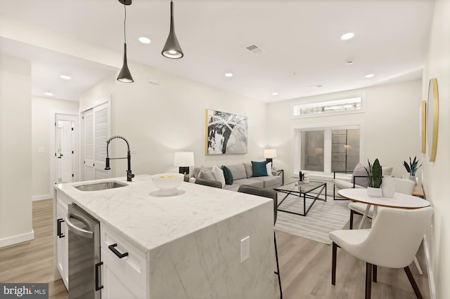 kitchen featuring visible vents, white cabinets, light wood-style flooring, decorative light fixtures, and a sink