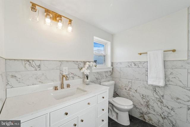 bathroom featuring a wainscoted wall, tile walls, toilet, vanity, and tile patterned flooring