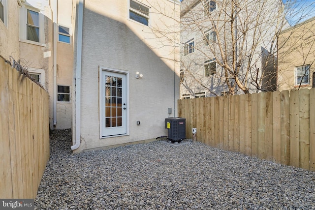 doorway to property featuring stucco siding, fence, and central AC unit