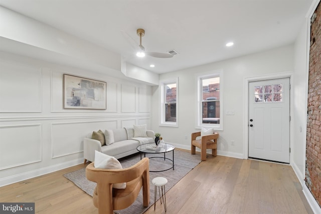 living room with visible vents, a decorative wall, light wood-style flooring, a ceiling fan, and baseboards