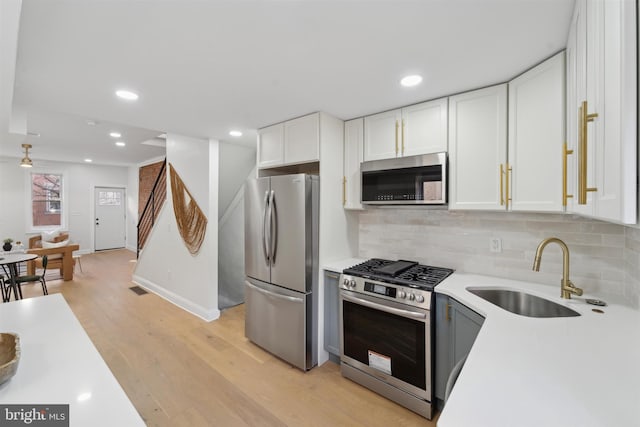 kitchen with light wood finished floors, light countertops, appliances with stainless steel finishes, white cabinets, and a sink