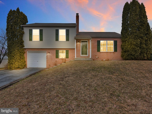 tri-level home with a garage, brick siding, driveway, and a lawn