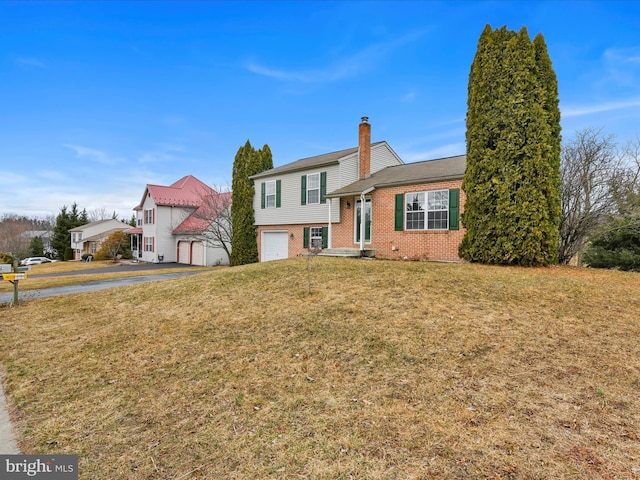 split level home featuring aphalt driveway, brick siding, a chimney, a front yard, and a garage