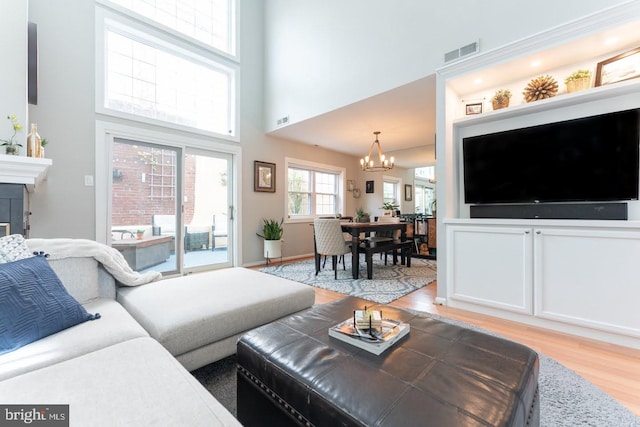 living area with a high ceiling, light wood-type flooring, visible vents, and a notable chandelier