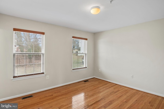 unfurnished room featuring baseboards, visible vents, and wood finished floors