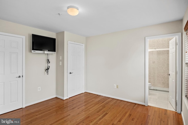 unfurnished bedroom featuring light wood-type flooring, baseboards, and ensuite bathroom