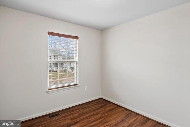 unfurnished room featuring baseboards, visible vents, and dark wood finished floors