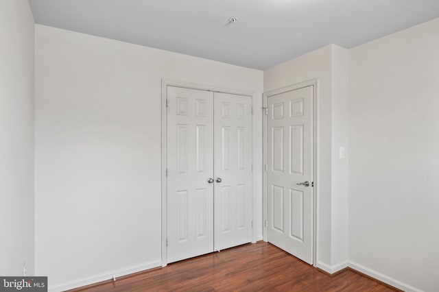 unfurnished bedroom featuring dark wood-style floors, a closet, and baseboards