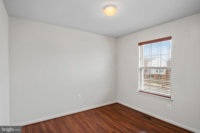 spare room featuring baseboards, visible vents, and dark wood finished floors