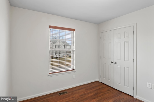 unfurnished bedroom with a closet, dark wood-style flooring, visible vents, and baseboards