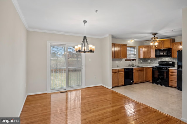 kitchen with light wood-style flooring, a sink, light countertops, decorative backsplash, and black appliances