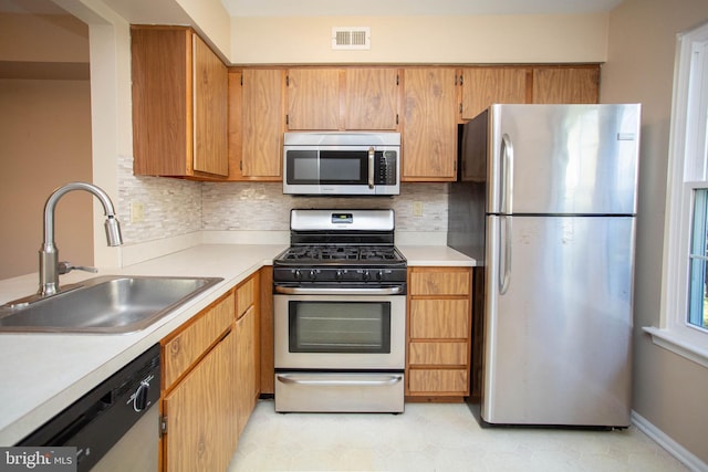 kitchen with tasteful backsplash, appliances with stainless steel finishes, light countertops, and a sink